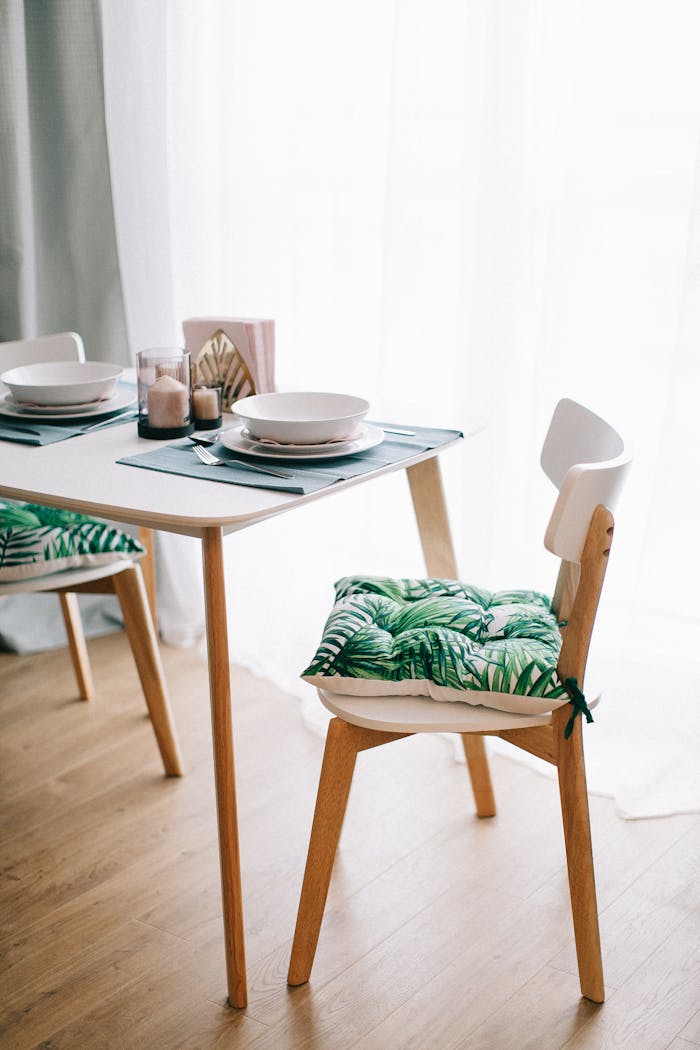 heros-img Contemporary dining room with wooden furniture and green-leaf cushions. Bright and inviting.