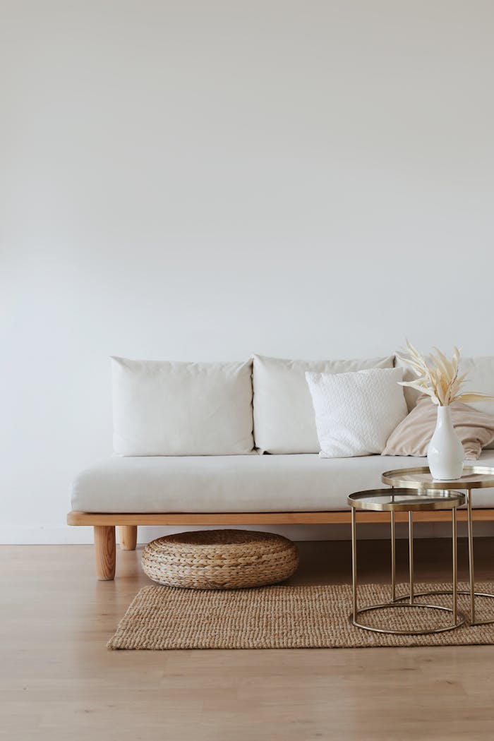 about-us A chic minimalist living room featuring a white sofa with cushions, dried flowers in a vase, and a wooden floor.